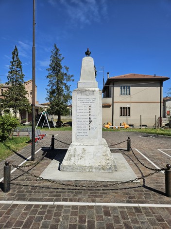Monumento ai Caduti di Pezzoli, eretto in memoria dei soldati, circondato da un'area verde e edifici storici.