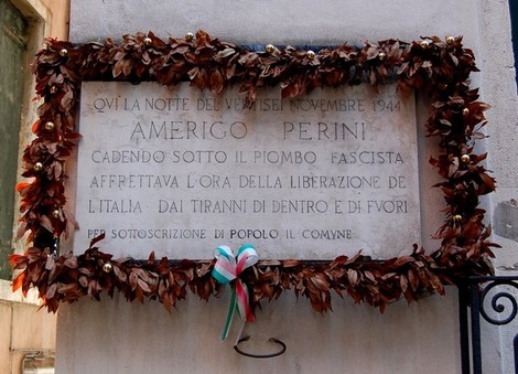 Lapide commemorativa ad Amerigo Perini, decorata con foglie e un nastro tricolore, in ricordo della liberazione.