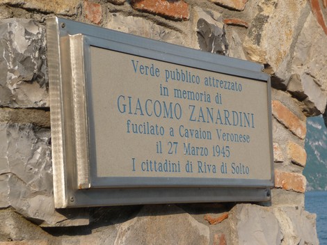 Lapide commemorativa di Giacomo Zanardini in un'area verde affacciata sul lago, con pietre e mattoni a vista.