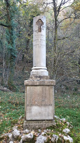 Monumento commemorativo dedicato a Rossi, Nocente e Olivieri, situato in un contesto naturale.
