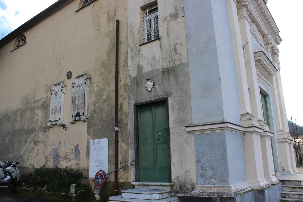 Lapide commemorativa e facciata di un edificio storico a Fontanegli, con segni di usura e vegetazione circostante.