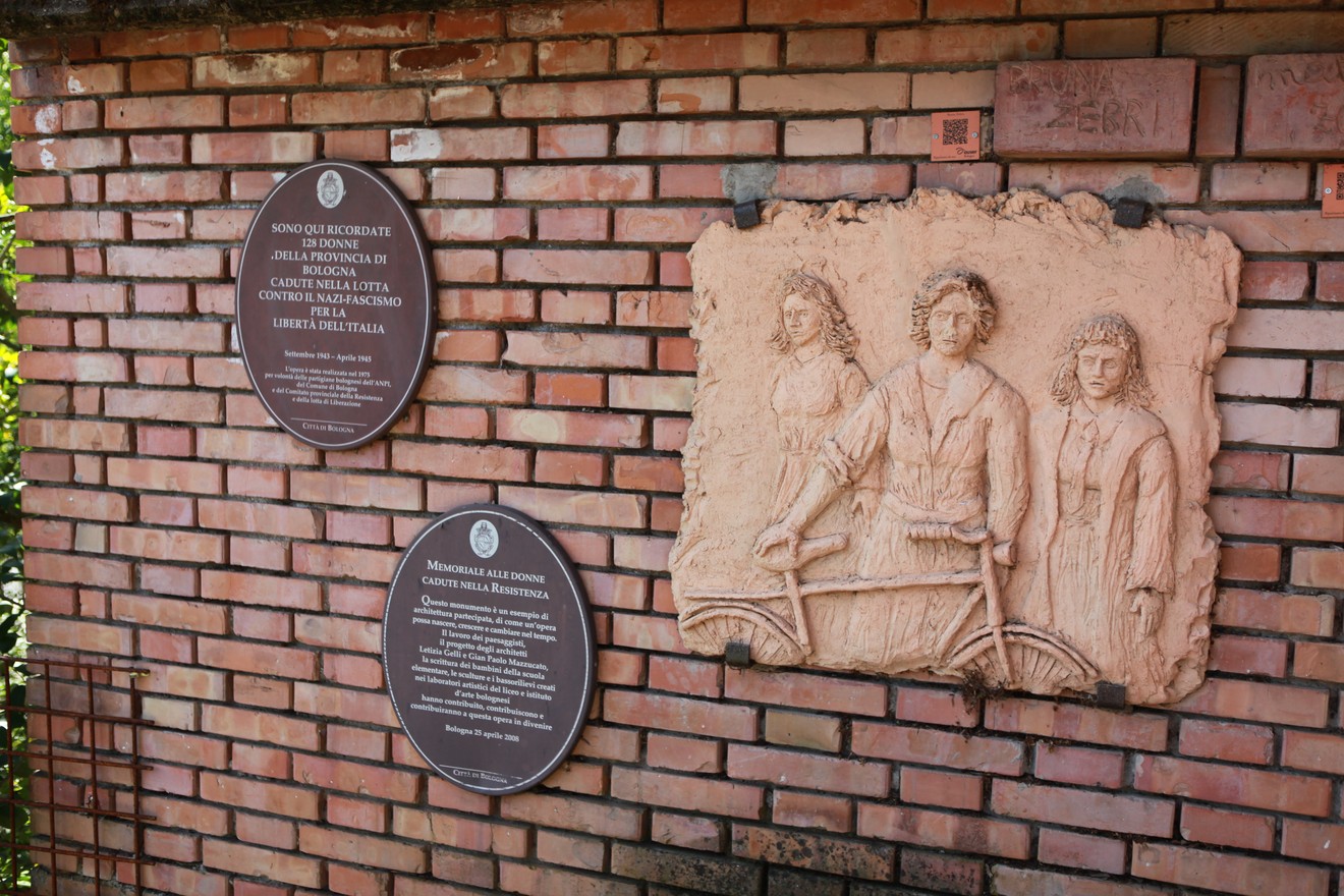 Monumento alle 128 partigiane, rappresentazione artistica e pannelli informativi su muro di mattoni.