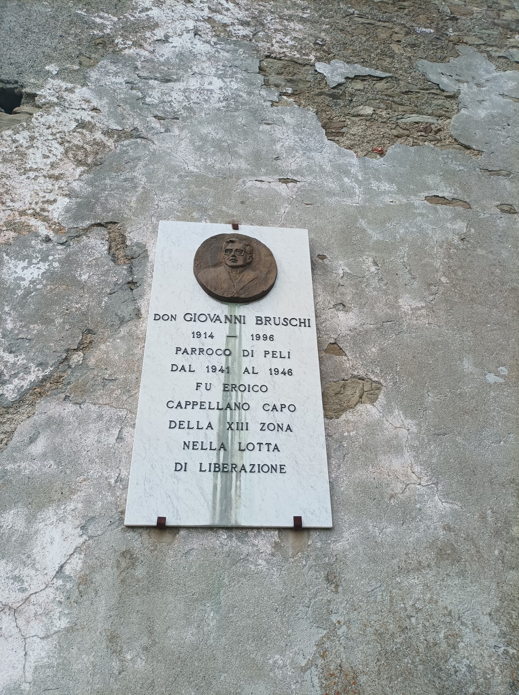 Lapide commemorativa di Don Giovanni Bruschi, con dettagli sulla sua vita e opera nella lotta di liberazione.