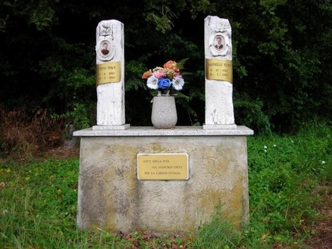 Monumento commemorativo dedicato a Conti e Mainelli, con fiori e statue su un basamento di pietra.