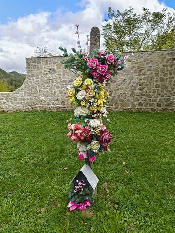 Cimitero di Casaglia: lapide decorata con fiori artificiali in un ambiente naturale e sereno.