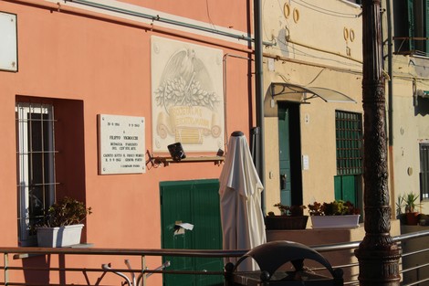 Lapide commemorativa su una parete colorata, con elementi architettonici circostanti.