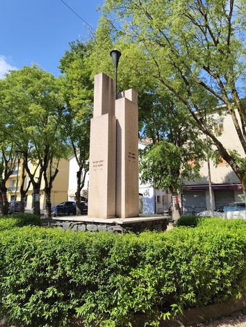 Monumento ai Caduti circondato da alberi e aiuole verdi, con una struttura in pietra prominente.