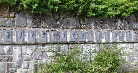 Monumento commemorativo ai partigiani, con medaglioni in rilievo su una parete di pietra.