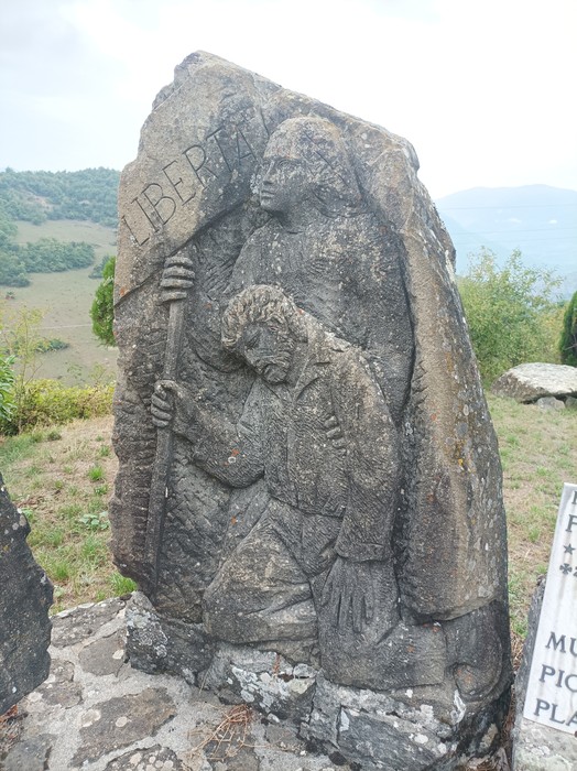 Monumento ai caduti con sculture che simboleggiano libertà e sacrificio, immerso in un paesaggio verde.
