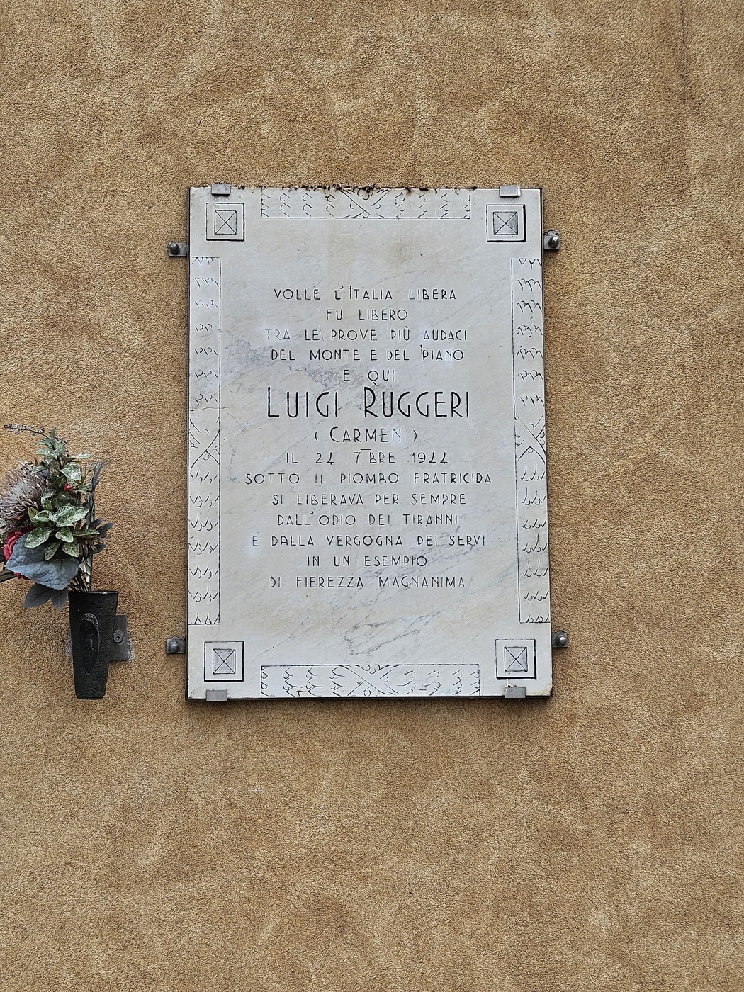Lapide commemorativa di Luigi Ruggeri, con decorazione floreale e scritte commemorative su sfondo murale.