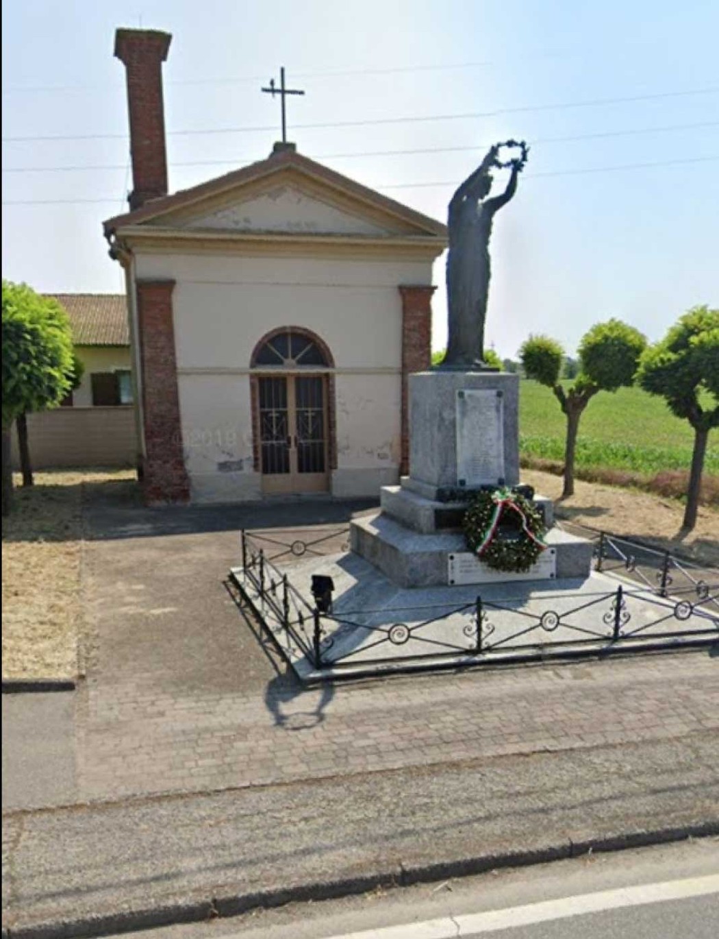Monumento ai caduti di Alagna, con statua e area commemorativa circondata da alberi e una cappella.