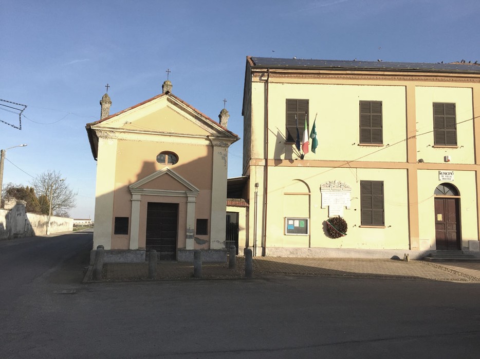 Lapide commemorativa per i caduti, situata a Villa Biscossi, con vista sulla chiesa e sull'edificio adiacente.