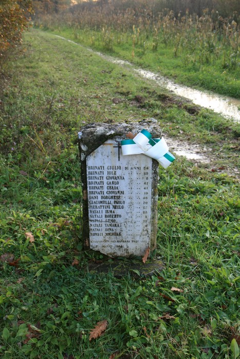 Cippo commemorativo dedicato alle famiglie Brinati e Natali, posizionato lungo un sentiero naturale.