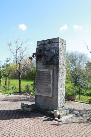Monumento ai caduti del Tiro a segno nazionale, con iscrizione su pietra e un albero dietro. Atmosfera serena e naturale.