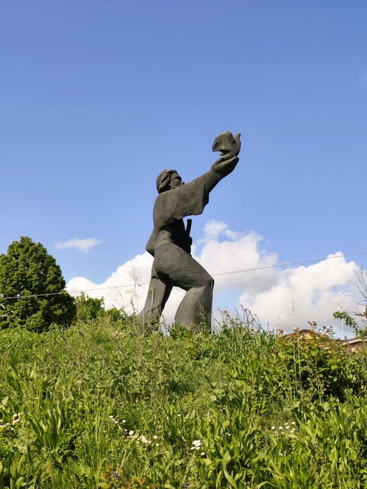 Monumento al Partigiano, statua bronzea che raffigura un combattente che alza un elmetto, circondato da vegetazione.