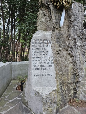 Monumento ai Caduti di San Canzian d'Isonzo, una pietra commemorativa immersa nella vegetazione.