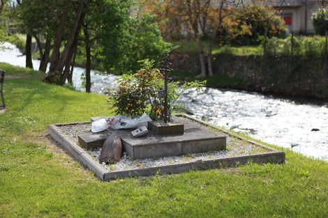 Monumento agli operai fucilati, circondato da alberi e un ruscello, con fiori freschi e una decorazione sobria.