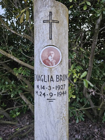 Cippo commemorativo con foto e date di nascita e morte, immerso in un contesto naturale.