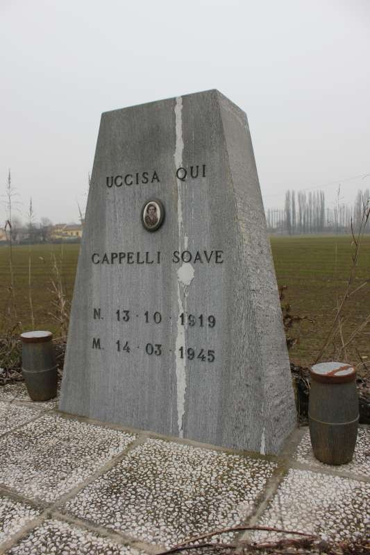 Cippo commemorativo in pietra dedicato a Cappelli Soave, situato in un campo. Atmosfera di rispetto e memoria.