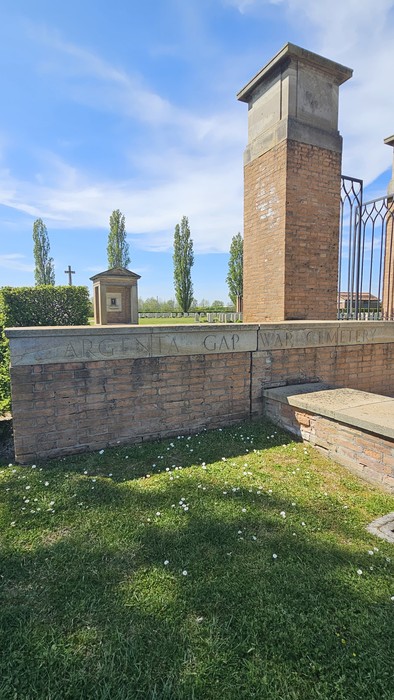 Cimitero di guerra Argenta Gap, con monumento e alberi sullo sfondo in una giornata di sole.