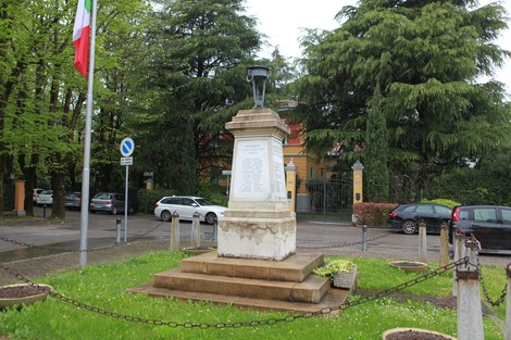 Monumento ai caduti per la Libertà, circondato da alberi e fiori, con bandiera italiana e lapidi commemorative.