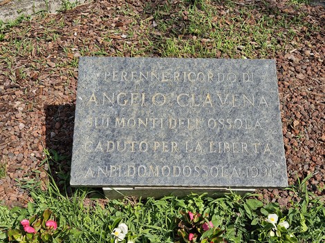 Monumento alla Resistenza con una targa commemorativa su un basamento circondato da fiori e vegetazione.