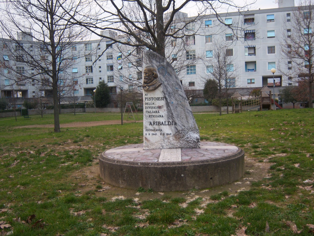 Monumento commemorativo della Divisione Garibaldi in un'area verde, con statue e iscrizioni suggestive.
