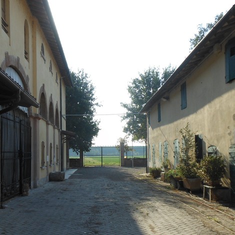 Viale di accesso a una storica struttura con edifici rustici e vegetazione circostante.