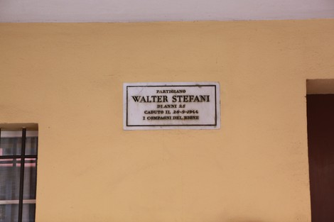 Lapide commemorativa dedicata a Walter Stefani, partigiano caduto nel 1944, affissa su un muro giallo.