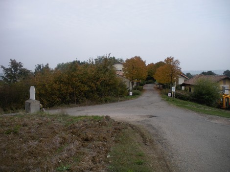 Cippo commemorativo a Villani e Rinaldi, con strada bianca e alberi autunnali sullo sfondo.