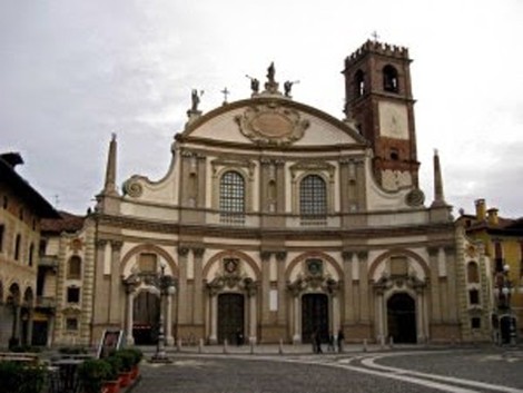 Facciata della Cappella a Olivelli, con dettagli architettonici e campanile, in un cielo nuvoloso.