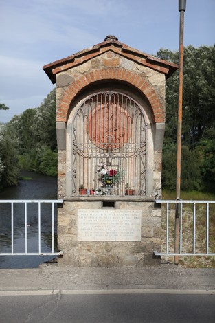 Lapide del ponte di Annibale, monumento storico con decorazioni e fiori, situato lungo un corso d'acqua.