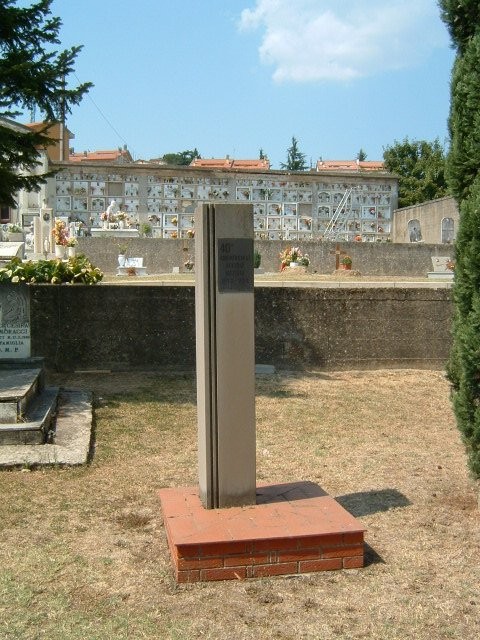 Cippo commemorativo nel cimitero di Meleto, circondato da tombe e loculi. Atmosfera di quiete e riflessione.