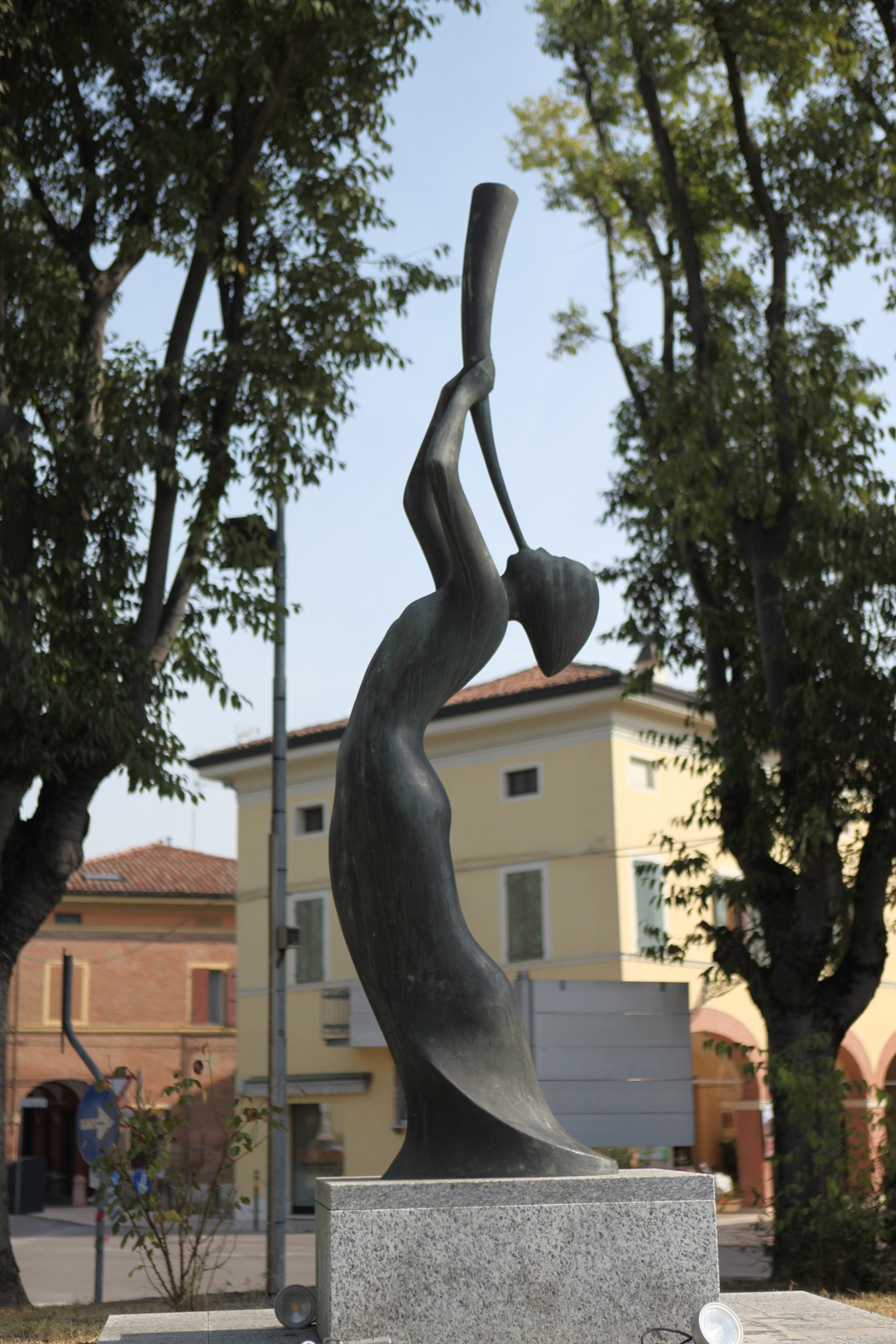 Monumento alle vittime del bombardamento, scultura evocativa tra alberi e edifici storici.