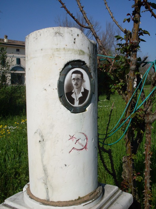 Cippo commemorativo con fotografia in un contesto verde, simbolo di memoria storica e radici locali.