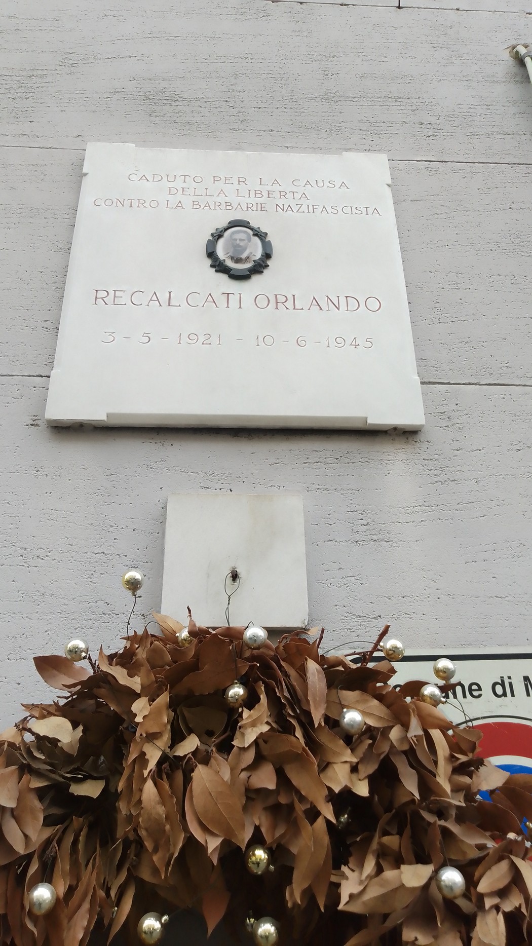 Lapide commemorativa in onore di Recalcati Orlando, con decorazioni floreali.