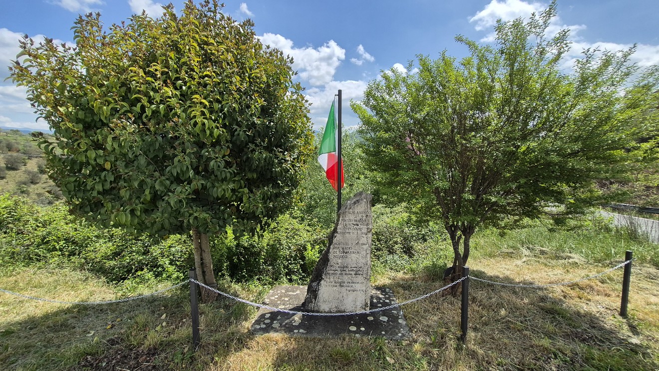 Monumento ai fucilati di Villa Spada, circondato da vegetazione e caratterizzato da una bandiera italiana.
