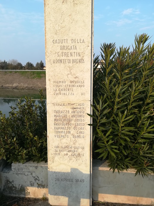 Cippo commemorativo ai caduti della Brigata Trentin, situato a Ponte di Brenta, circondato da vegetazione.