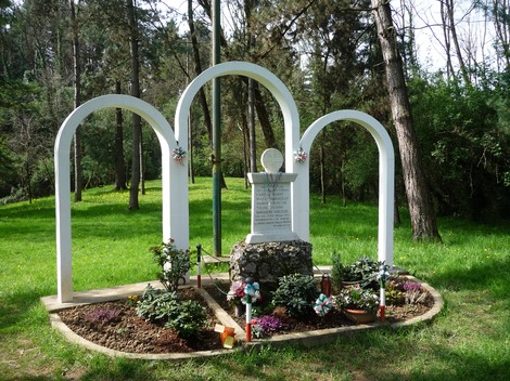 Monumento ai Caduti partigiani, circondato da archi bianchi e verdeggiante vegetazione.
