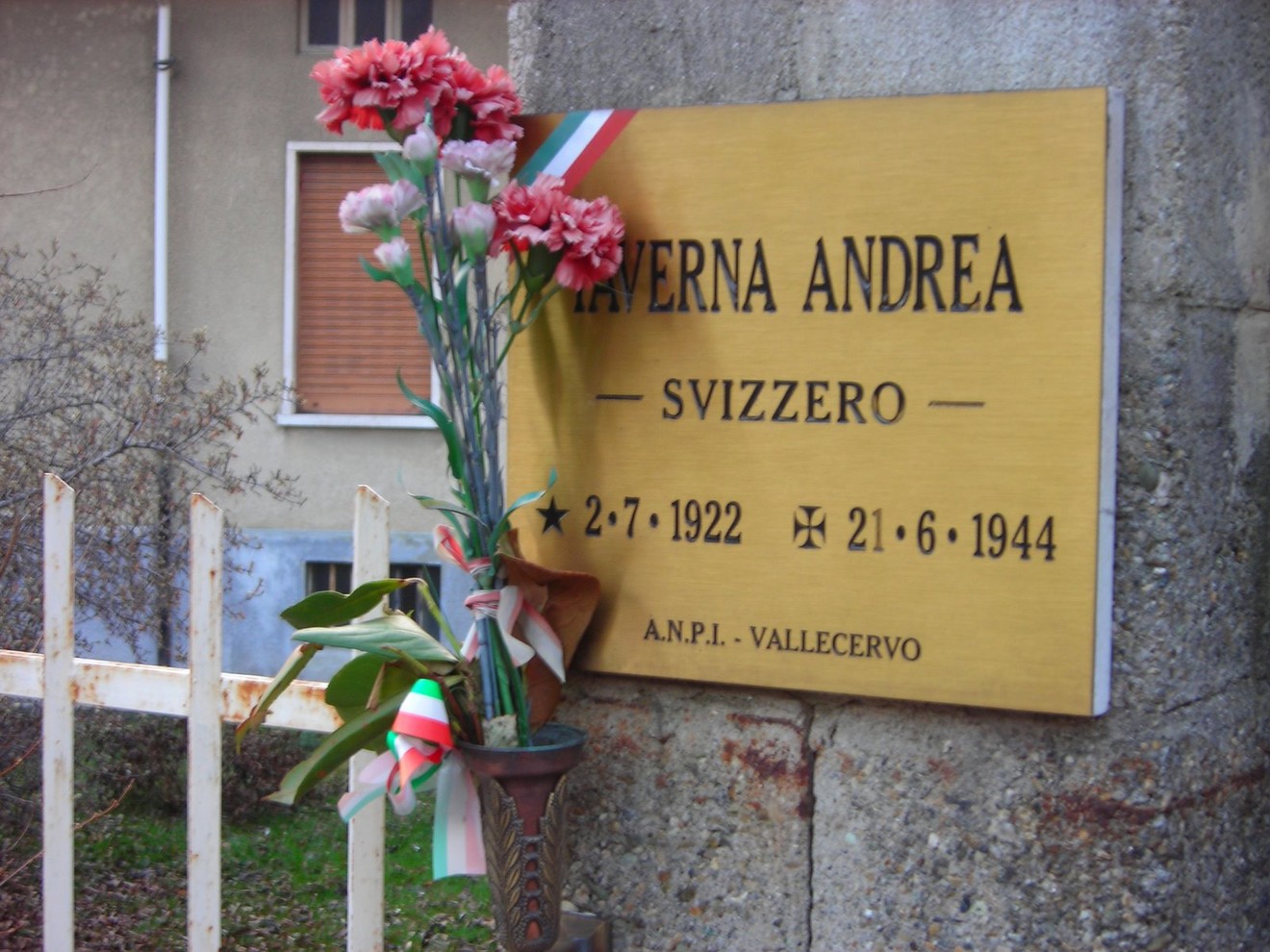 Targa commemorativa dedicata a Taverna Andrea, testimone di eventi storici. Fiori e decorazioni tricolore in omaggio.