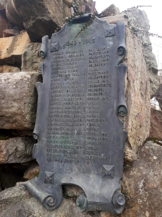 Monumento ai caduti, una scultura imponente con iscrizioni commemorative su fondo di pietra.