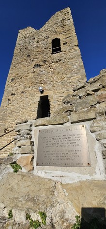 Targa commemorativa a Ricciardelli, situata accanto a una torre storica, sotto un cielo blu.