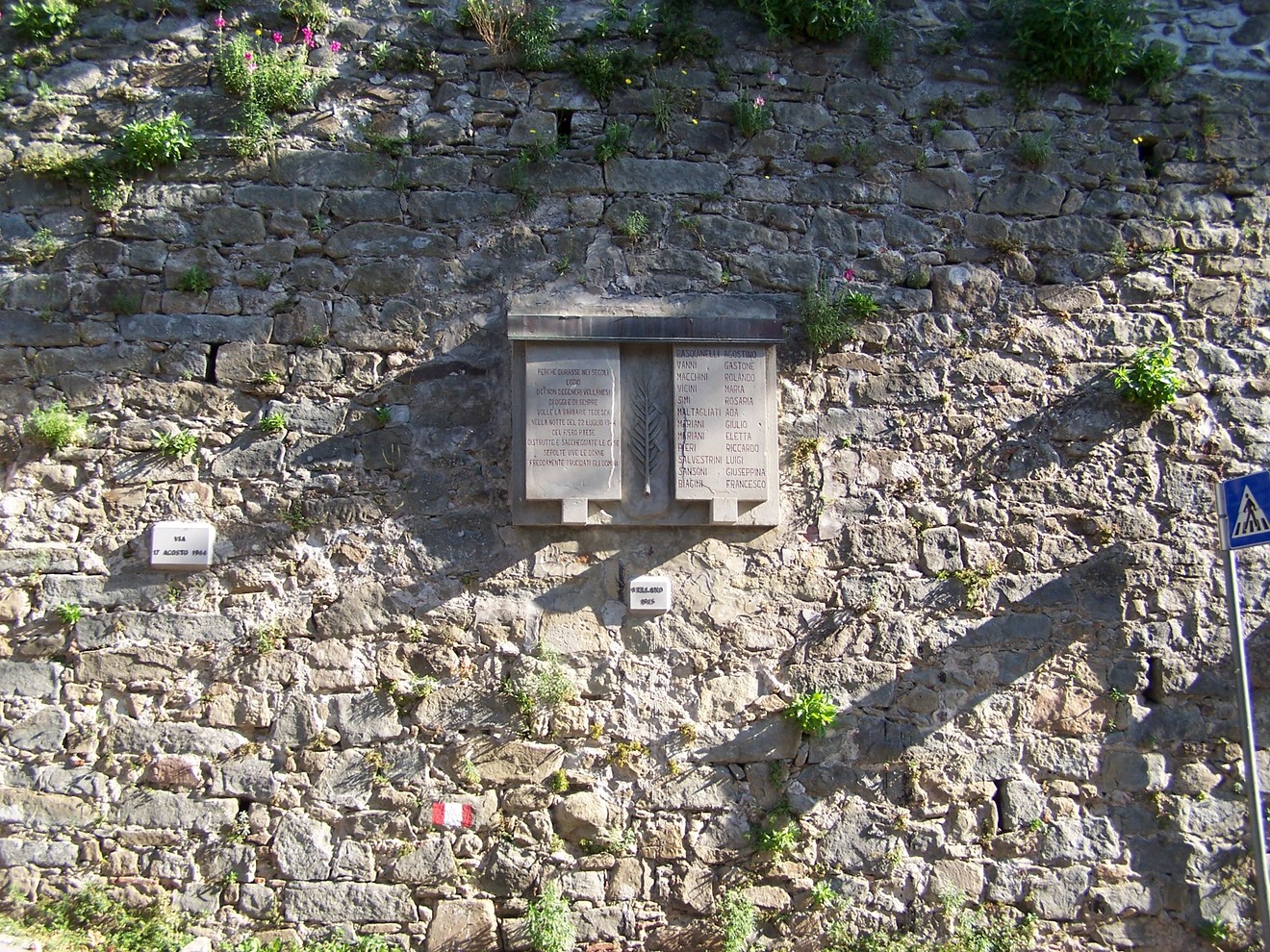 Lapidi di Vellano, commemorative, fissate su una parete di pietra, circondate da vegetazione.