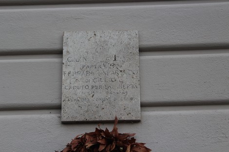 Lapide commemorativa dedicata a Ferradini, affissa su una parete con un prato di foglie secche sottostante.