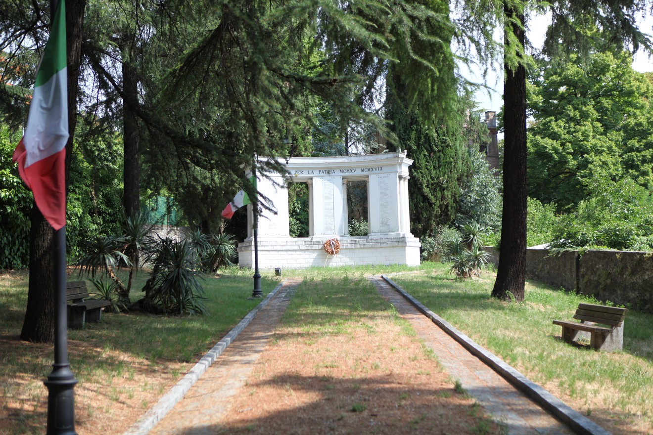 Monumento ai Caduti immerso nel verde, con bandiere italiane e un sentiero che conduce al monumento.