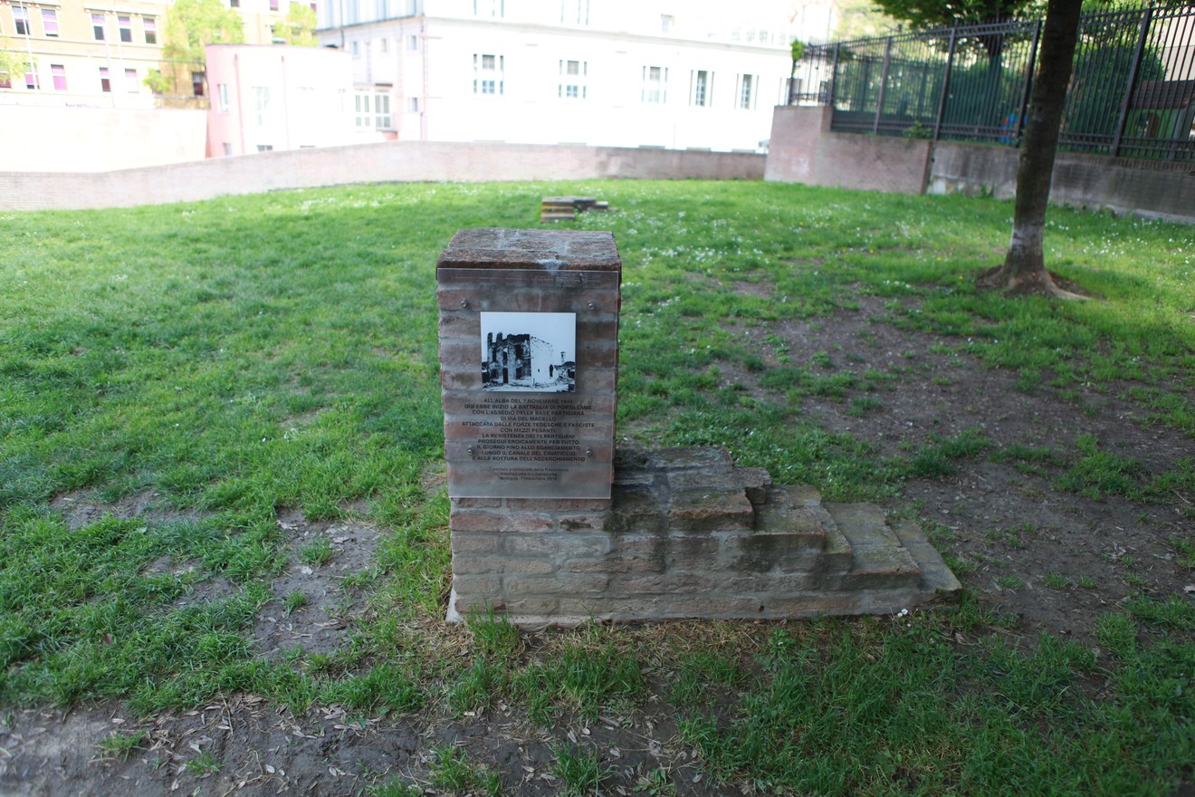 Targa commemorativa alla base partigiana di Porta Lame, situata in un'area verde e circondata da edifici.