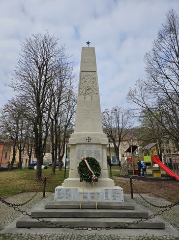 Monumento ai Caduti di Vezzano sul Crostolo con obelisco e corona d'alloro, circondato da alberi e parco giochi.