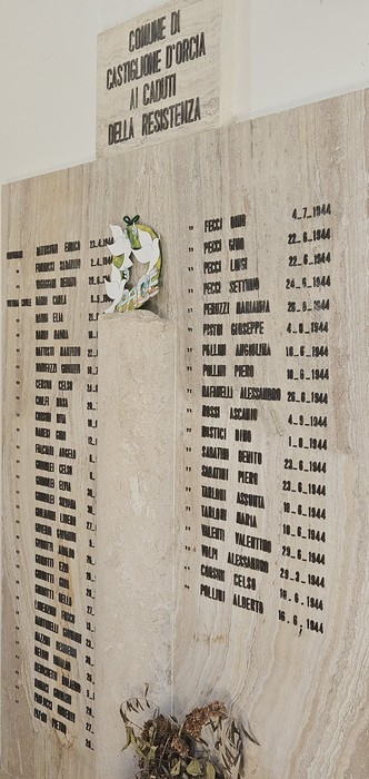 Lapide in pietra con lungo elenco di nomi e date, decorata con un mazzo di fiori sotto il cartiglio superiore.