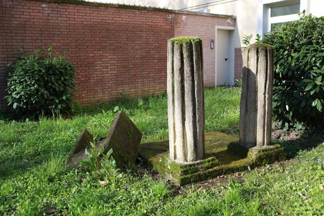 Monumenti in pietra con colonne, circondati da vegetazione e muffa, rappresentano la Resistenza.