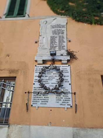 Lapide commemorativa con nomi dei caduti e una corona di alloro, affissa su una parete.